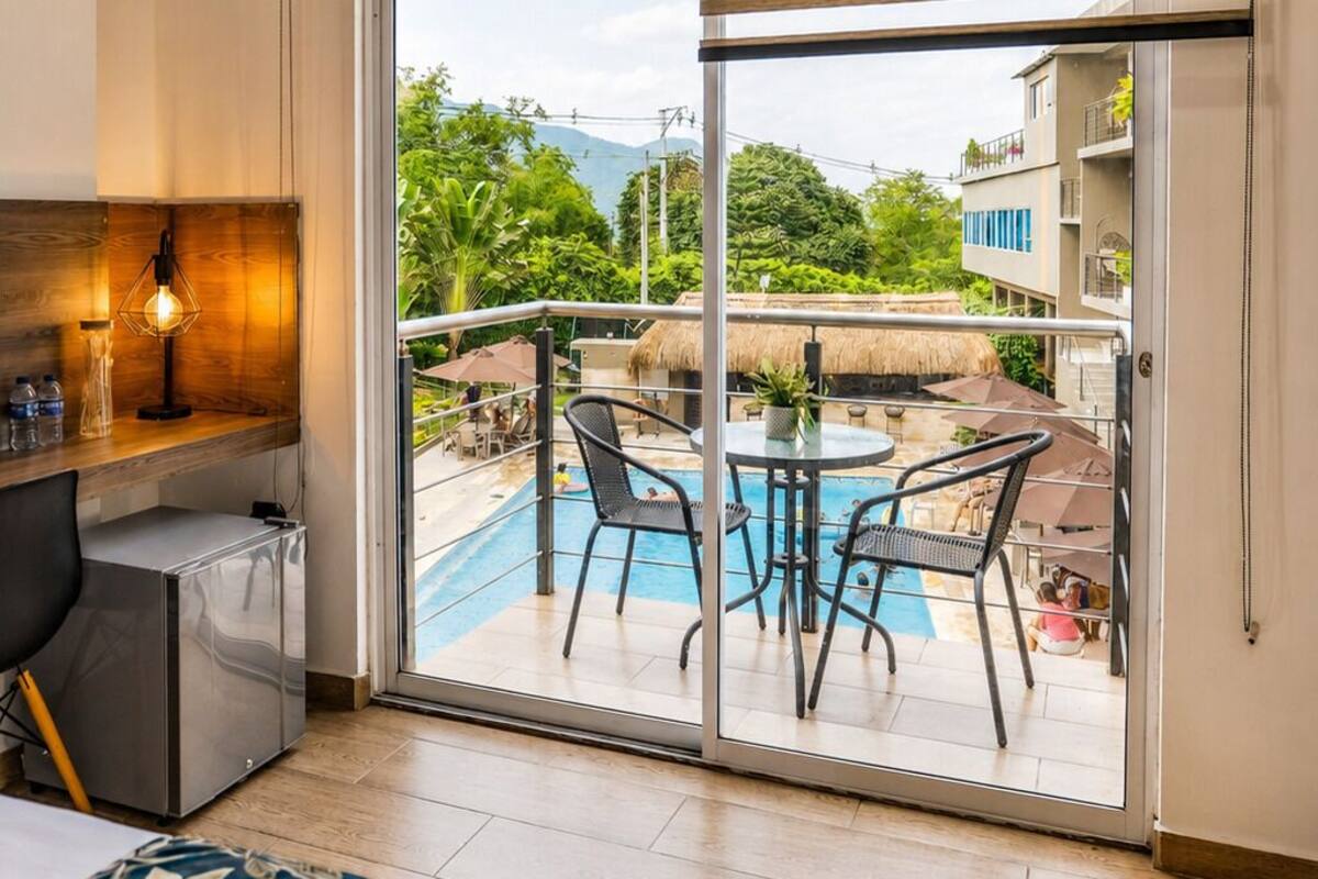 Een hotelkamer met balkon, zwembad en bed.