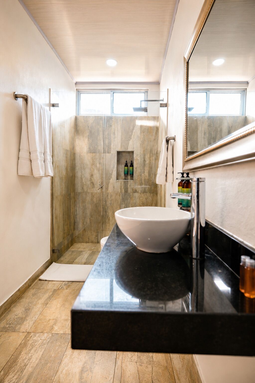 Un baño moderno con un lavamanos grande de color blanco, una encimera negra, zona de ducha y un espejo.