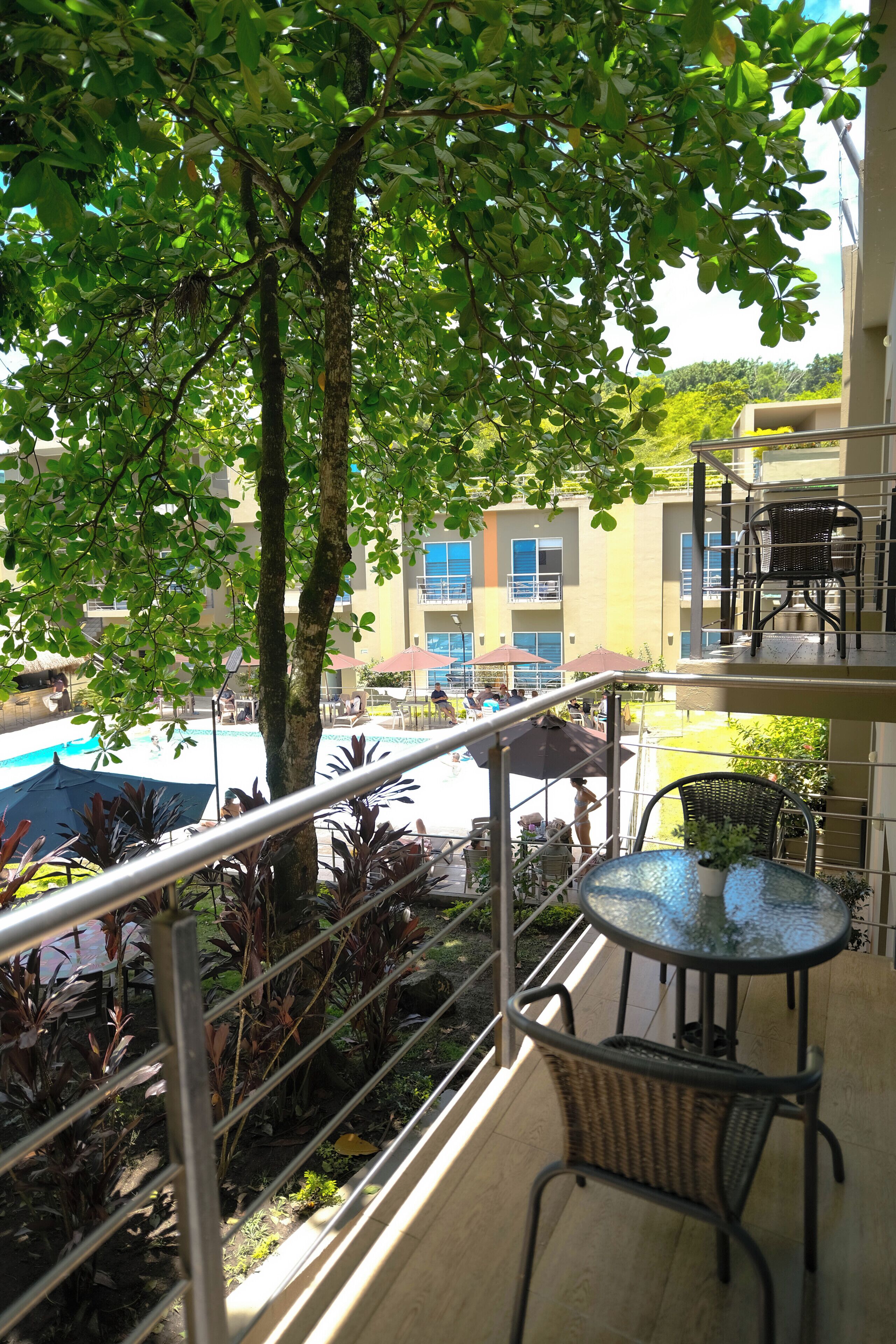 A balcony with a table and chairs, a view of a swimming pool, and a building in the background.