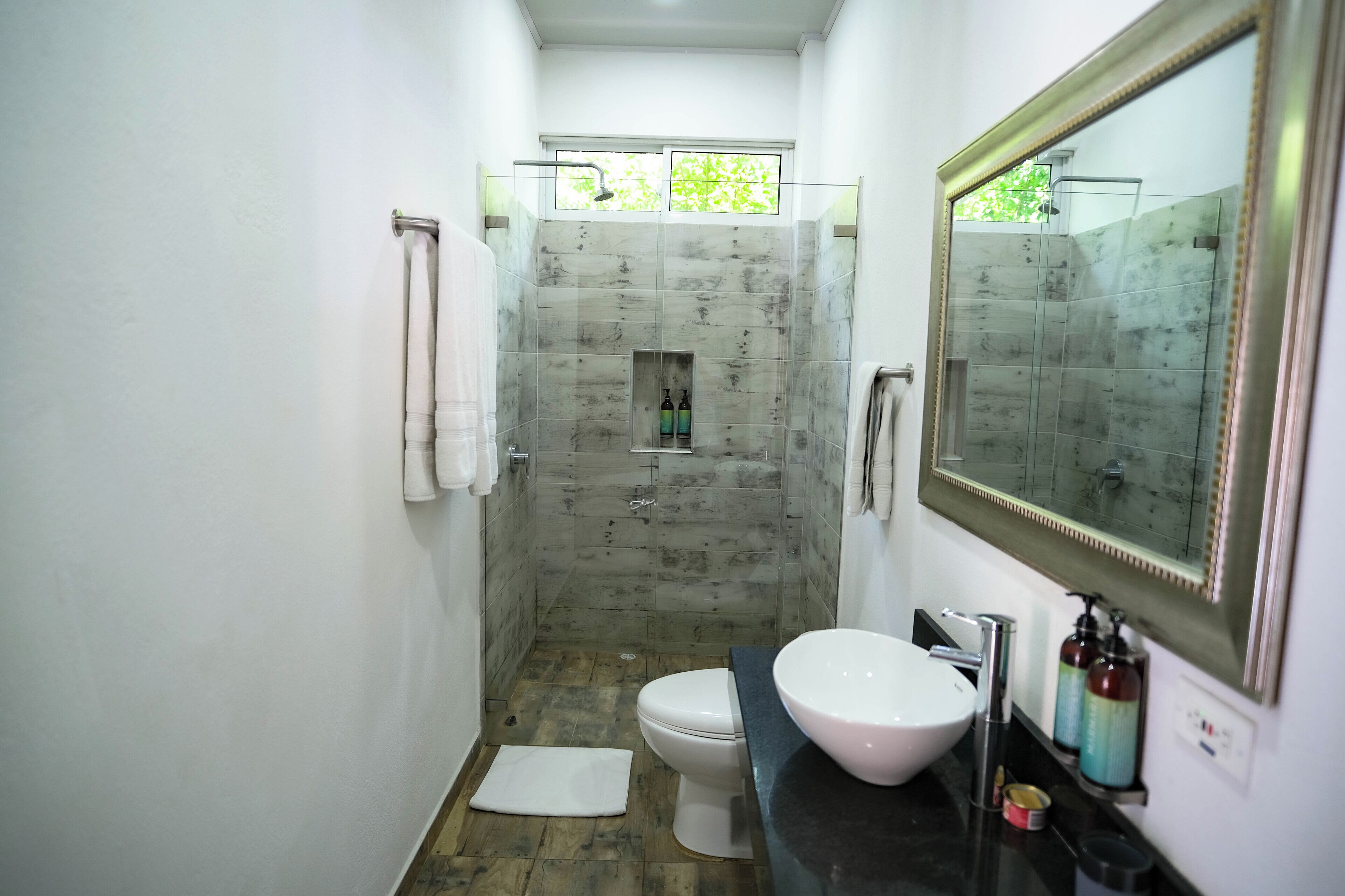 Un baño con ducha, inodoro, lavabo y un espejo grande.