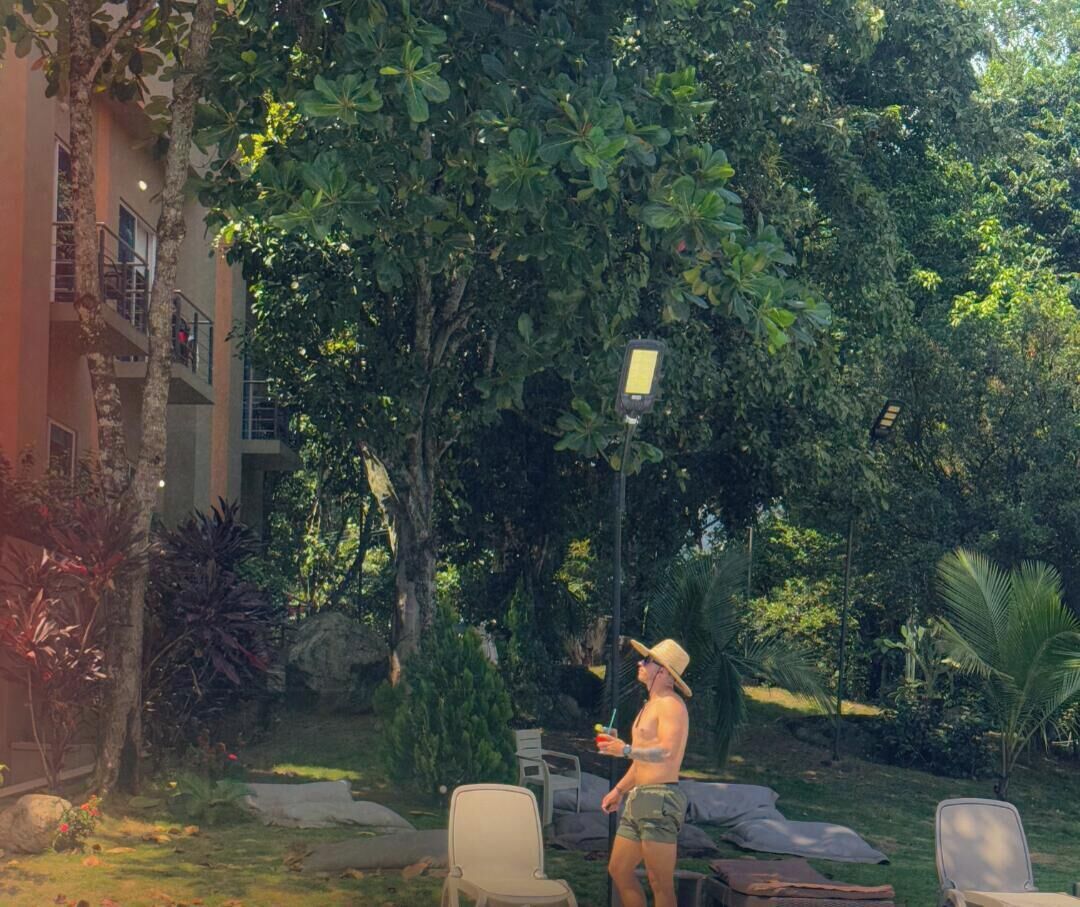 Una persona de pie en un jardín con árboles y un edificio al fondo.