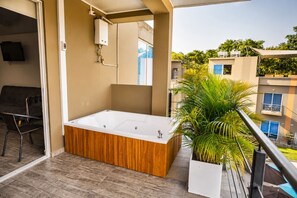 Un balcon avec une baignoire en bois, une plante en pot et une vue sur les bâtiments voisins.