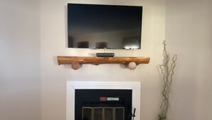 Una sala de estar con chimenea, un televisor montado encima y un cubo rojo en el suelo.