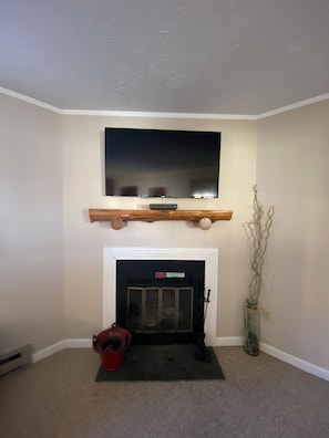 A living room with a fireplace, a television mounted above it, and a red bucket on the floor.