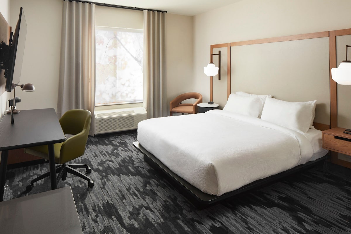 Une chambre d’hôtel avec un grand lit, un bureau avec une chaise, une petite table et une lampe.