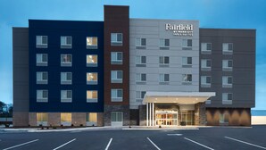 A multi-story hotel with a modern facade, featuring a prominent entrance with a covered area and a parking lot in front.
