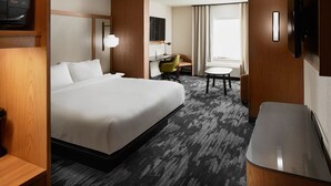 A hotel room with a large bed, a desk, a chair, a TV, and a small table.