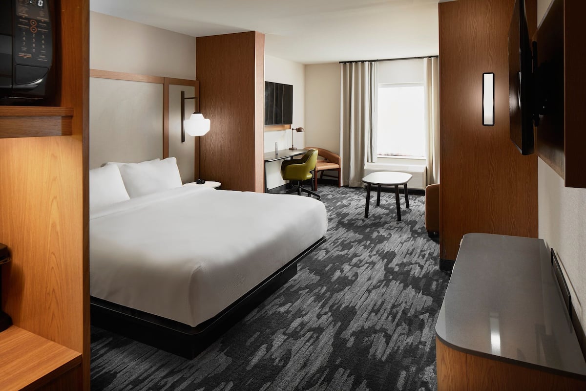 Une chambre d’hôtel avec un grand lit, un bureau, une chaise, une télévision et une petite table.
