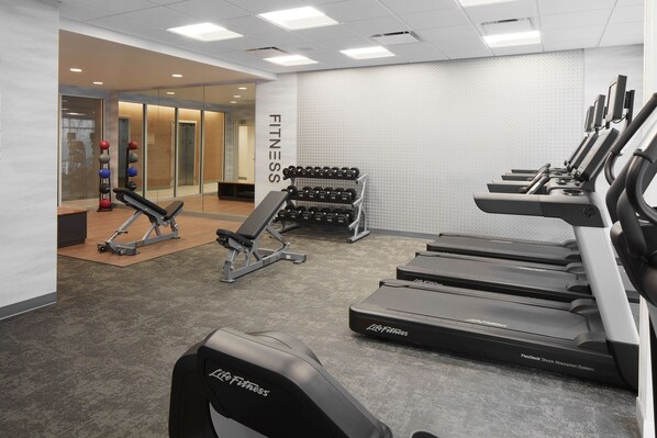 A gym with treadmills, dumbbells, and a bench.
