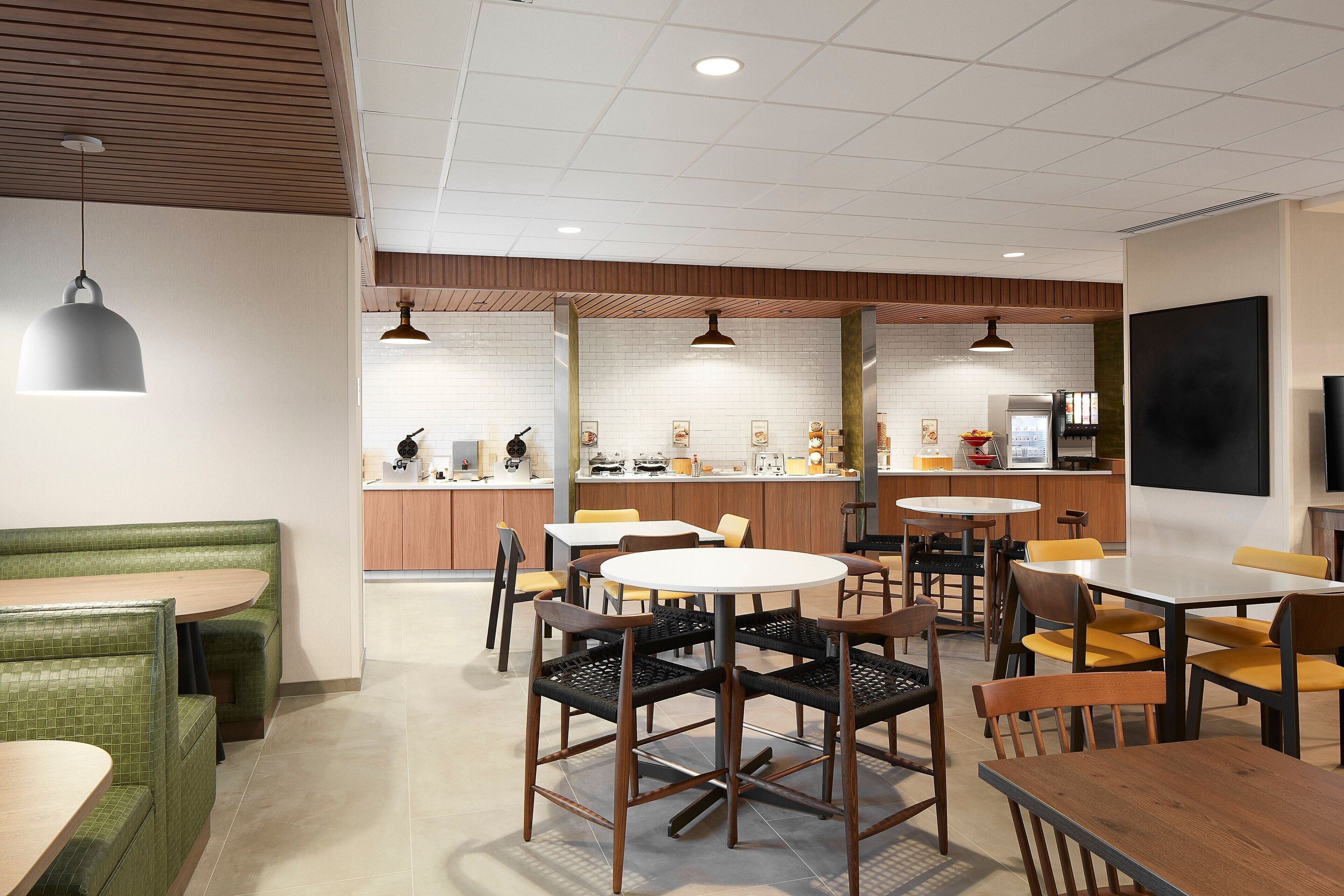 A modern restaurant with booths, round tables, and chairs.