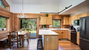 Een moderne keuken met houten kastjes, een centraal eiland, roestvrijstalen apparatuur en grote ramen met uitzicht op de omgeving.