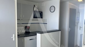 A compact kitchen with a microwave, a clock, and a refrigerator.