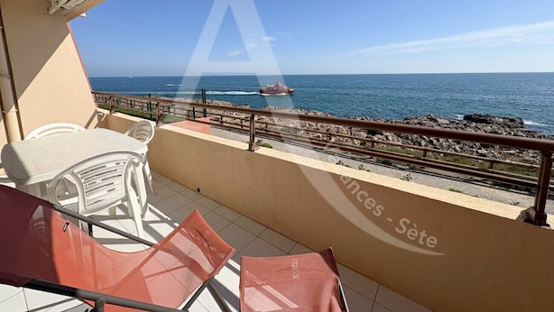 A balcony with a view of the sea, a table, and two chairs.