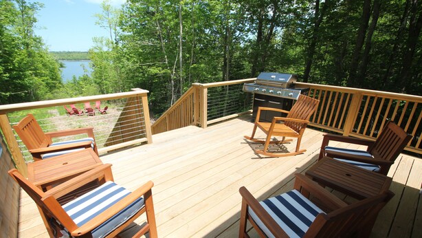 A wooden deck with outdoor furniture, a grill, and a view of a lake surrounded by trees.