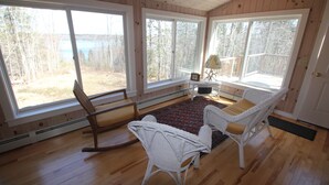 A room with large windows, wooden flooring, and wicker furniture.