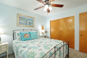 Ein Schlafzimmer mit einem Bett, einem Deckenventilator, einer Tür und einem Bild an der Wand.