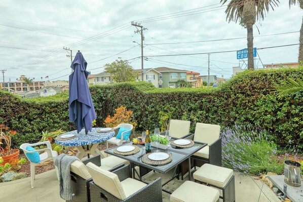 Eine Terrasse im Freien mit einem Esstisch, umgeben von Korbstühlen und einem blauen Sonnenschirm.