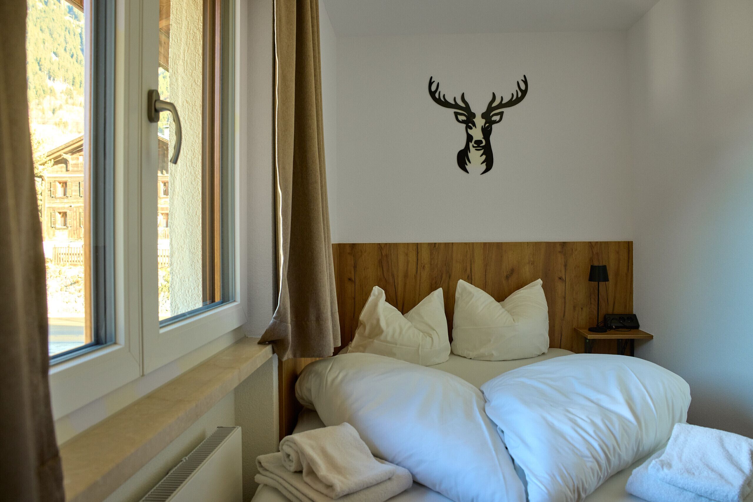 A hotel room with a bed, a headboard, a nightstand, a lamp, and a window with curtains.