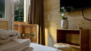 Una habitación de madera con una cama, un taburete pequeño, una estantería con un jarrón y un televisor en la pared.
