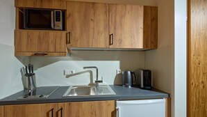 Una cocina con armarios de madera, un lavamanos de acero inoxidable, un microondas, un hervidor y un tostador.
