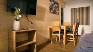 Una habitación de madera con un televisor montado en la pared, una mesa de comedor con sillas y una cama con ropa blanca de cama.