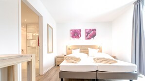 Une chambre moderne avec un lit double, une tête de lit en bois, des tables de chevet et deux œuvres d’art florales accrochées au mur.