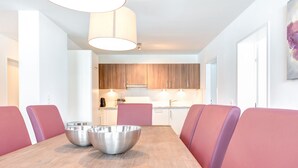 Un espace repas moderne avec une table en bois, des chaises à revêtement rose et un grand saladier en métal.