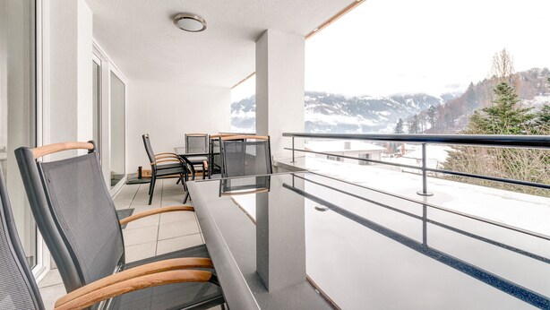 Un balcon donnant sur des montagnes enneigées, une table avec des chaises et une rambarde.