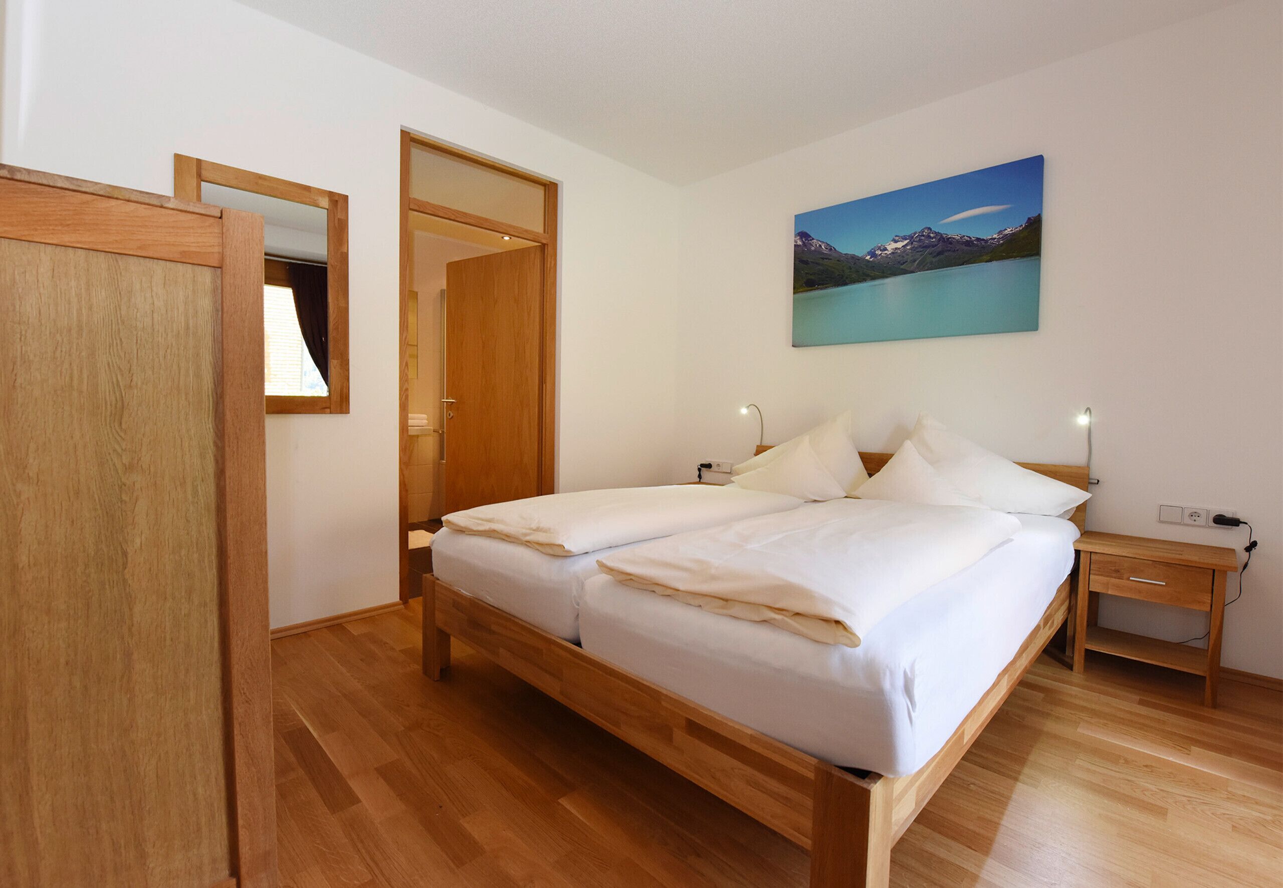 Une chambre à coucher avec un lit en bois, une table de chevet, un tableau accroché au mur et une armoire en bois.