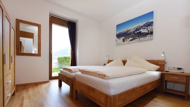 Een slaapkamer met een houten bed, nachtkastje, spiegel en een raam met uitzicht op bergen.