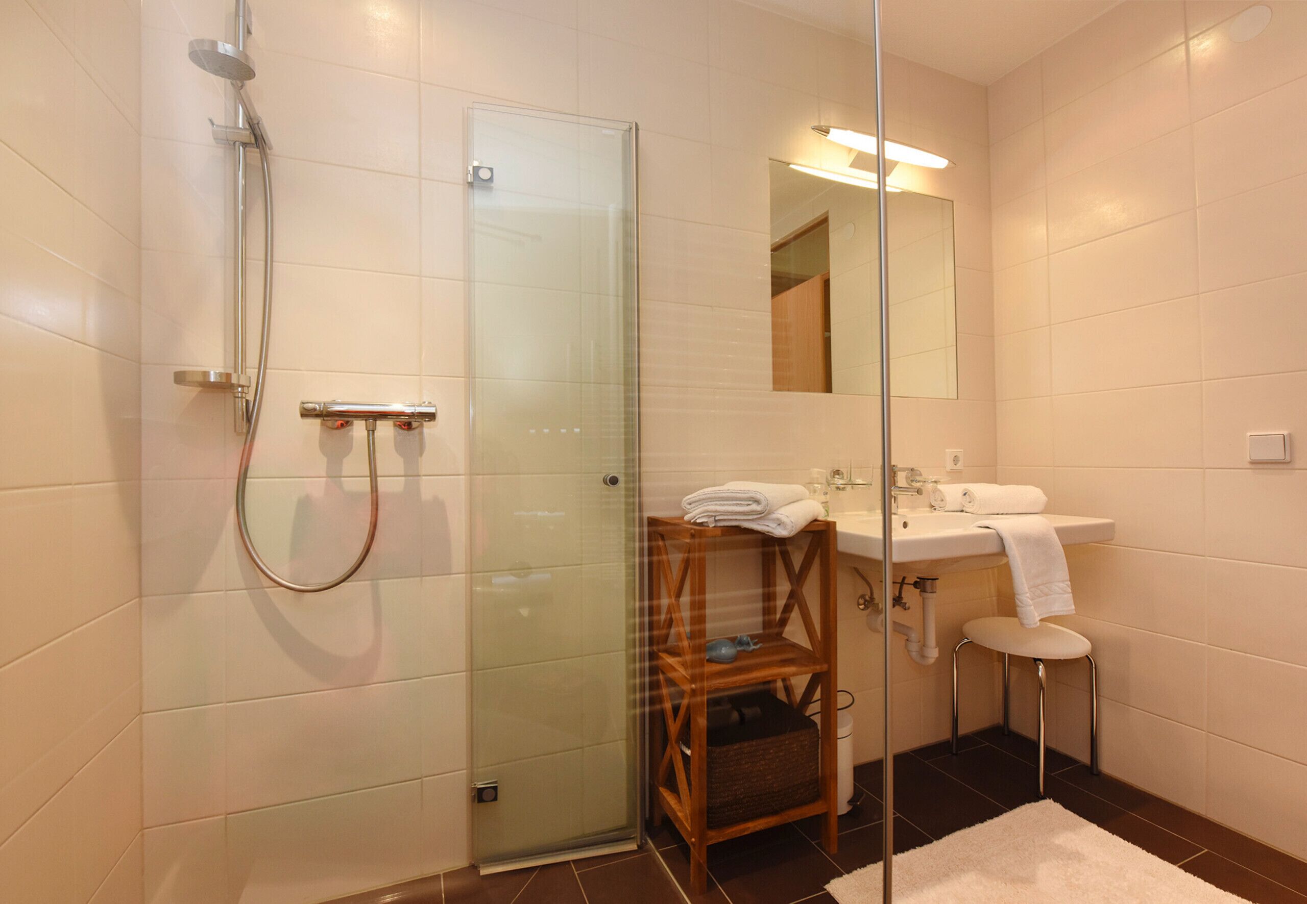 Une salle de bain moderne avec une douche à parois de verre, une étagère en bois avec des serviettes, un lavabo et un miroir.