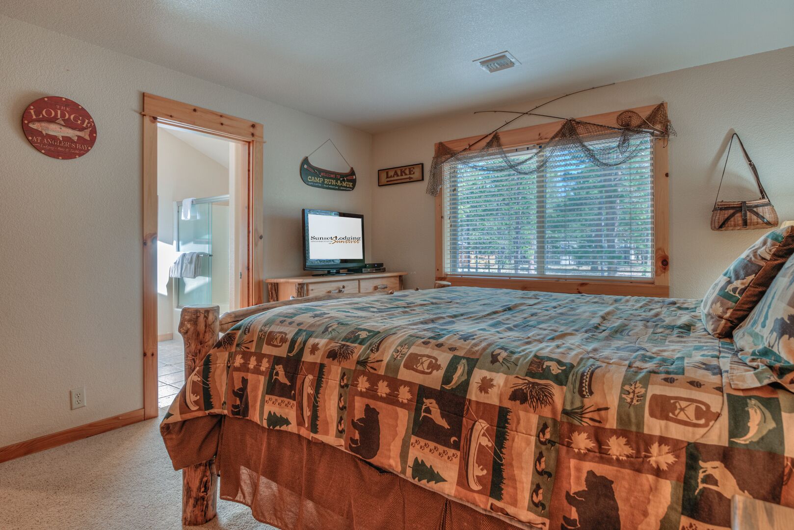 A bedroom with a large bed, a television, a window with blinds, and a door leading to another room.