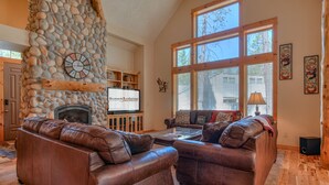 Una sala de estar acogedora con chimenea de piedra, sofás de cuero y ventanas amplias.