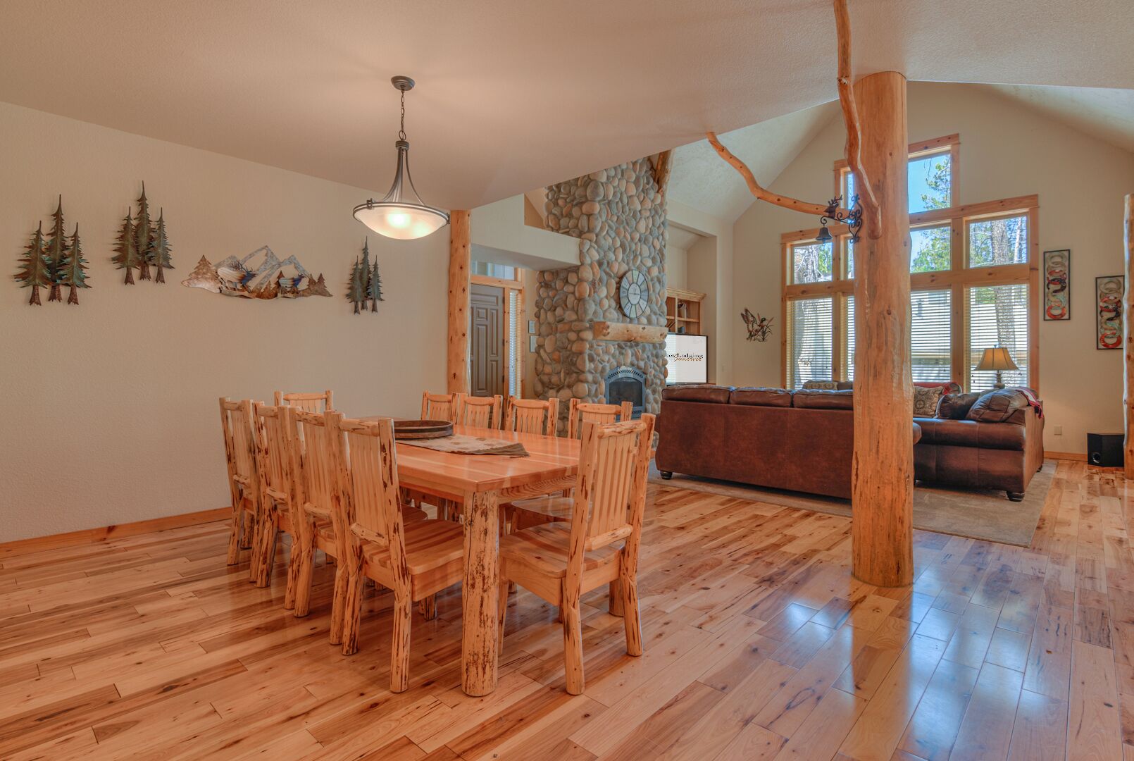 Un vaste espace de vie comprenant une table et des chaises en bois pour la salle à manger, une cheminée en pierre et une grande fenêtre équipée de stores.