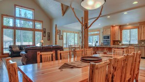 Un comedor amplio con una mesa y sillas de madera, un gran candelabro y vistas a la cocina al fondo.