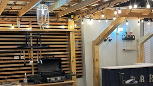 Tunnelmallinen, maalaishenkinen sisustus, jossa on baaritiski, puupöytiä ja grilli.
