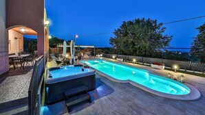 A swimming pool with a hot tub, outdoor seating, and a view of the sea at dusk. - Villa Lioness in Kastel Luksic, playground & pool (Kastel Luksic)