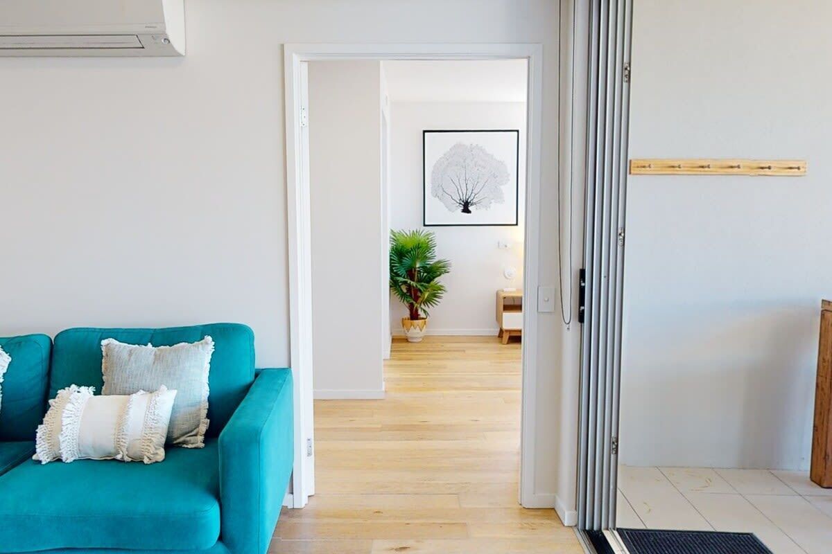 A teal sofa with decorative pillows, a framed artwork on the wall, and a wooden floor.