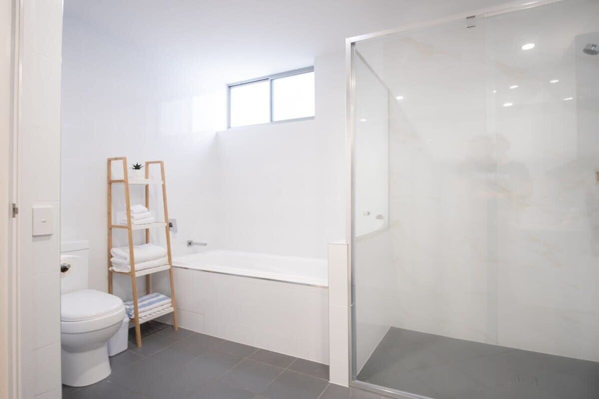 A modern bathroom with a toilet, a shower enclosure, a bathtub, and a shelf with towels.