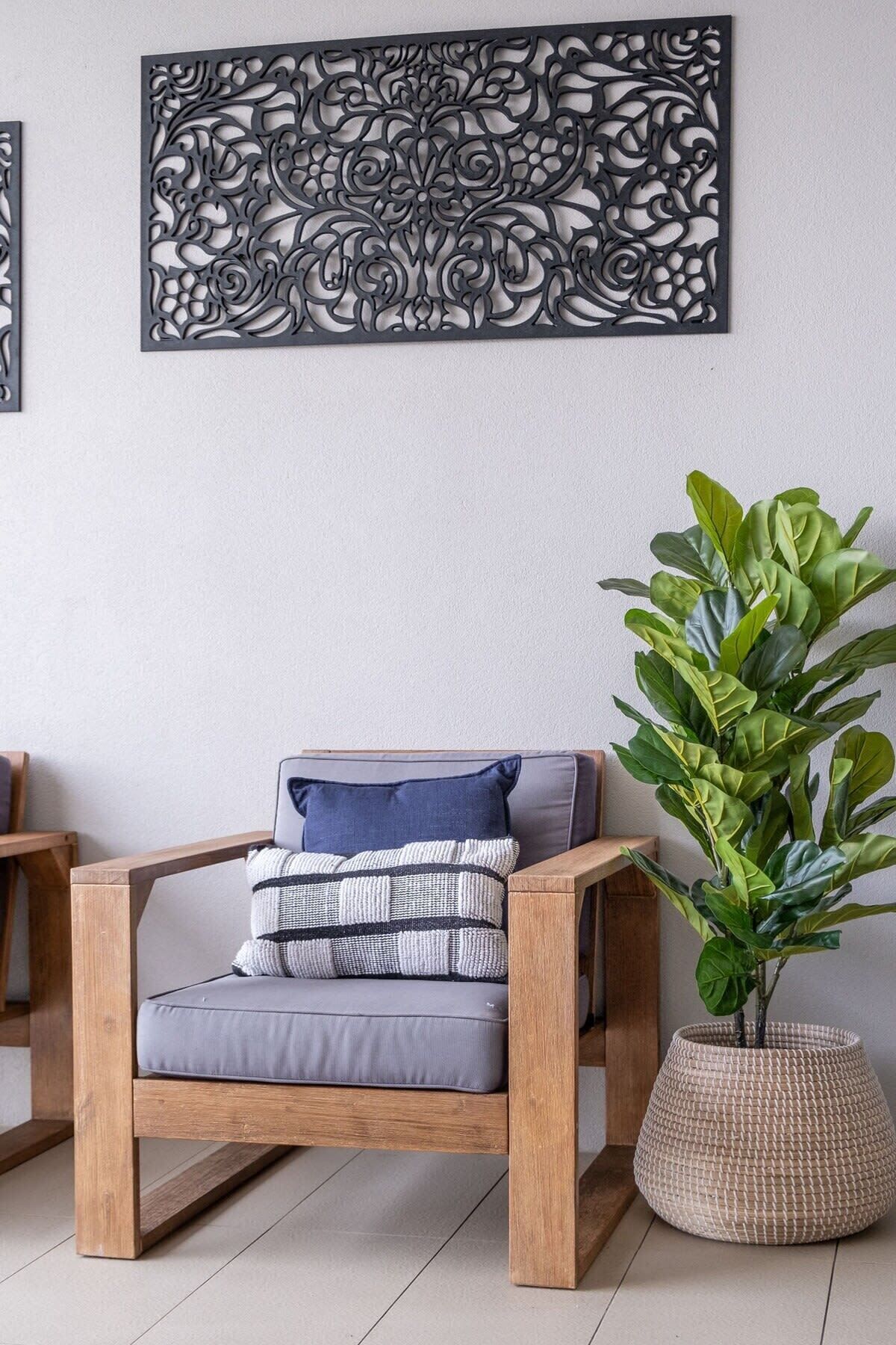 Une chaise en bois avec des coussins, une grande plante en pot et un élément décoratif mural.