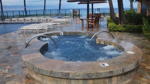 A hot tub with a stone surround, a poolside area with lounge chairs, and a view of the ocean. - Mahana 604 Oceanfront 1bd/1ba 1 Bedroom Condo by RedAwning (Lahaina)