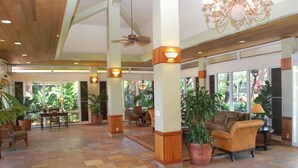 A spacious lobby with a tiled floor, wooden pillars, and a ceiling fan. There are several potted plants and a sofa in the seating area. - Mahana 604 Oceanfront 1bd/1ba 1 Bedroom Condo by RedAwning (Lahaina)