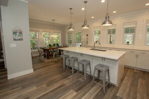 A spacious kitchen with a large island, bar stools, pendant lighting, and a view of the outdoors.
