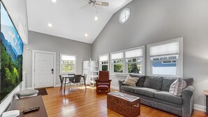 A spacious living room with hardwood floors, a gray couch, a wooden coffee table, and a television. - Cozy cottage NOW available for short or long term rentals(seasonal) (Michigan City)