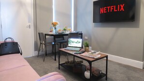 A hotel room with a bed, a desk with a laptop, a TV mounted on the wall, and a window with a view. - Tudors eSuites Three Bedroom House (Coventry)