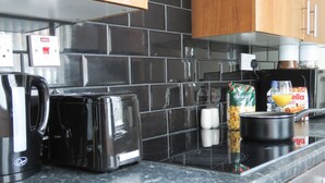 A kitchen with black tiled backsplash, a coffee maker, a kettle, and a box of cereal. - Tudors eSuites Three Bedroom House (Coventry)