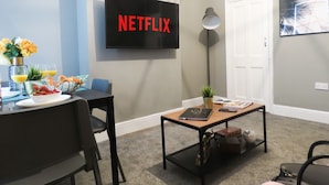 A modern living room with a flat-screen TV mounted on the wall displaying "NETFLIX". - Tudors eSuites Three Bedroom House (Coventry)