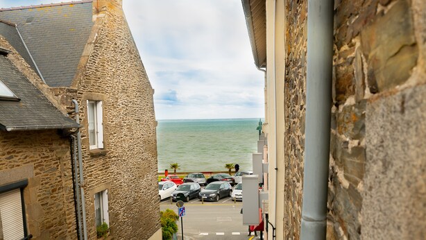 A narrow street with stone buildings, a parking lot, and a view of the sea.