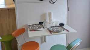 A dining area with a white table, two chairs, a television, and a wall-mounted shelf.