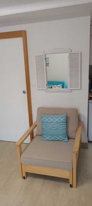 Una habitación con una silla de madera, un cojín, un espejo en la pared y una puerta.